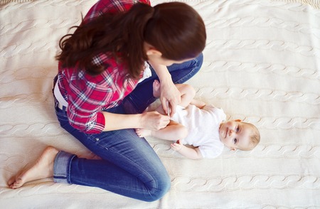 Cute little baby girl getting dressed by her mother on a carpet in a living room.