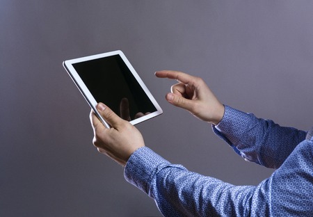 Unrecognizable young hipster with his tablet. Studio shot on gray background.
