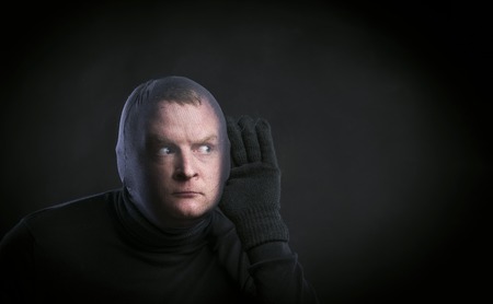Thief in action with balaclava on his face, dressed in black. Studio shot on black background.