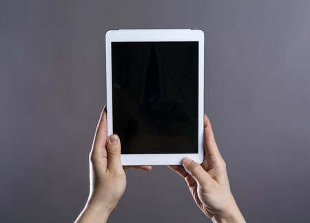 Unrecognizable young hipster with his tablet. Studio shot on gray background.