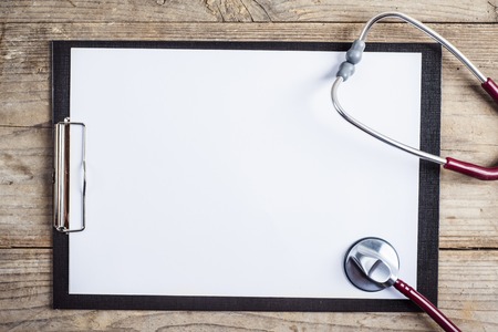 Workplace of a doctor. Stethoscope and clip board on wooden desk background.
