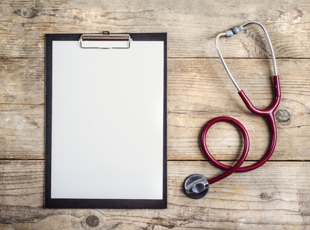 Workplace of a doctor. Stethoscope and clip board on wooden desk background.の写真素材