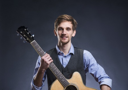 Young handsome guitar player. Studio shot on black background.