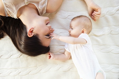 Cute little baby girl and her mother lying on a knitted blanket.の写真素材
