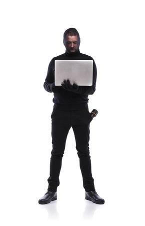 Thief in action stealing information with balaclava on his face, dressed in black. Studio shot on white background.の写真素材