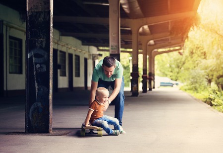 Cute little boy with his father on a skateboard in the city