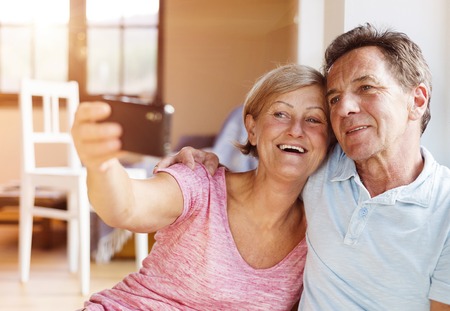 Happy senior couple taking selfie in their living room.の写真素材