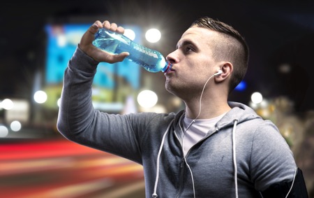Young sportsman jogging in the night city with a water bottleの写真素材