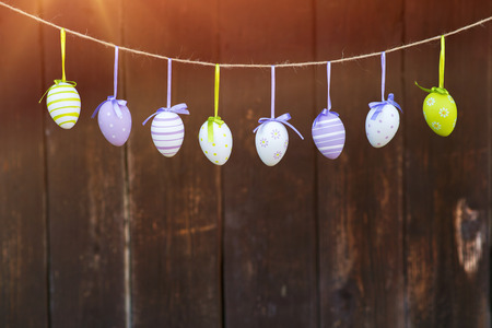 Colorful easter eggs hanging on a twine at the wooden wall background.の写真素材