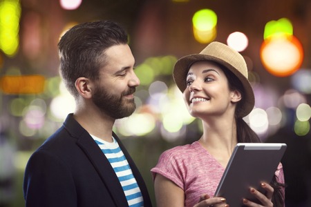 Trendy young hipster couple with a tablet enjoying nightlife in the cityの写真素材
