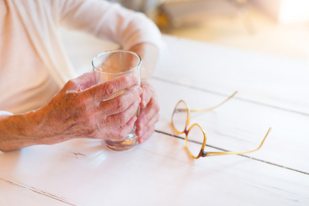 Hands of unrecognizable senior woman holding a glass of waterの写真素材