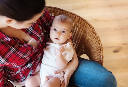 Mother sitting in a chair holding her little baby girl in her arms.の写真素材