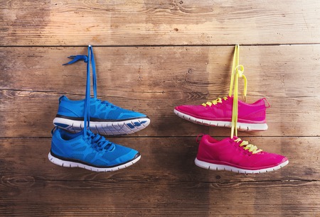 Two pairs of sneakers hang on a nail on a wooden fence background
