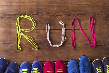 Five pairs of running shoes and shoelaces run sign on a wooden floor background