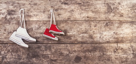 Two pairs of sports shoes hang on a nail on a wooden fence backgroundの写真素材