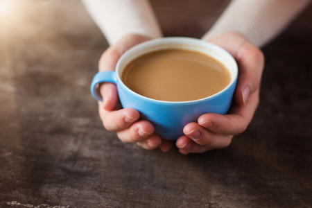 Unrecognizable woman holding a cup of coffee on a wooden table の写真素材