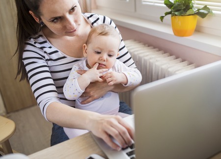 Young mother in home office with computer and her daugherの写真素材