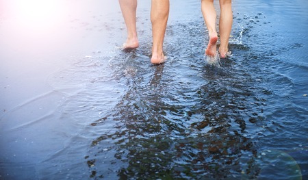 Unrecognizable woman and man walking barefoot through a puddle