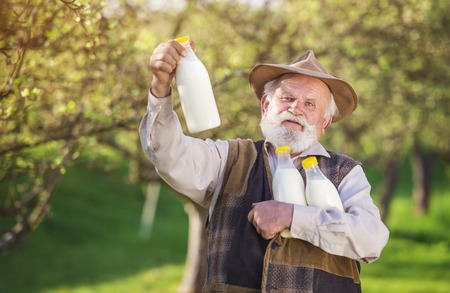 Senior farmer with milk bottles outside in green natureの写真素材