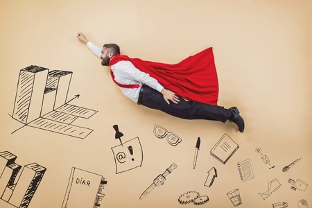 Manager in a superman pose wearing a red cloak. Studio shot on a beige background.の写真素材
