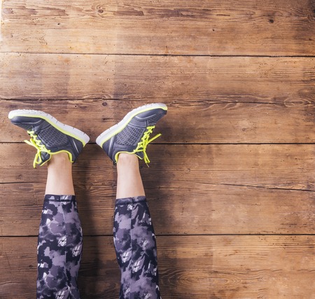Unrecognizable young runner sitting on a floor. Studio shot on wooden background.の写真素材