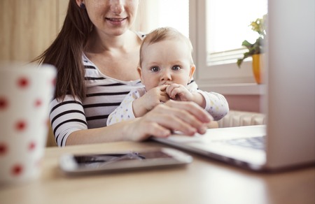 Young mother in home office with computer and her daugherの写真素材