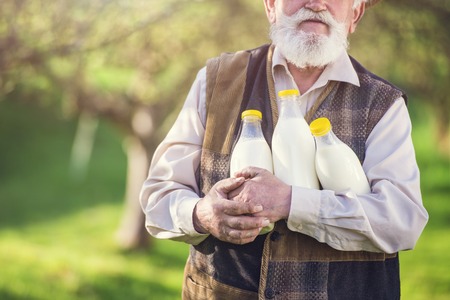 Senior farmer with milk bottles outside in green natureの写真素材