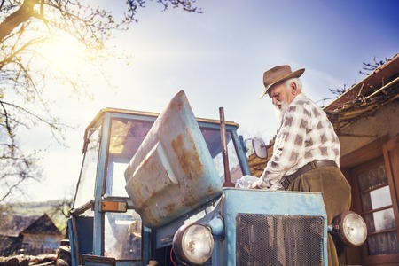 Senior man at the farm repairing an old tractorの写真素材