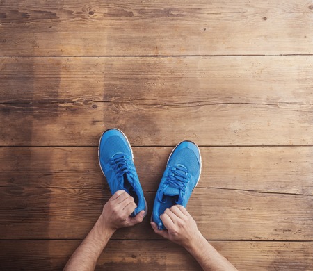 Man holding a pair of running shoes on a wooden floor backgroundの写真素材