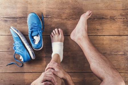 Unrecognizable injured runner sitting on a wooden floor background