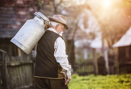 Senior farmer carrying kettle for milk on his backの写真素材