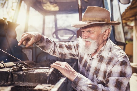 Senior man at the farm repairing an old tractorの写真素材