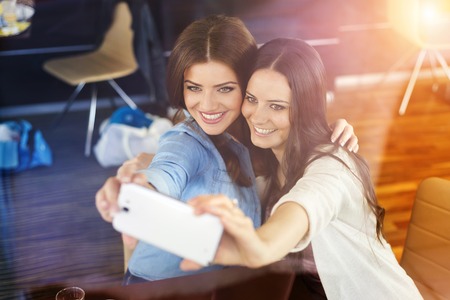 Two beautiful women taking selfie in cafeの写真素材