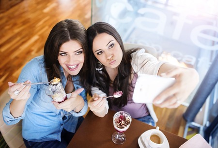 Two beautiful women taking selfie in cafeの写真素材