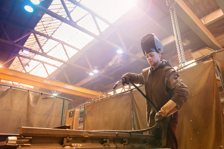 Young man with protective mask welding in a factory