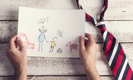 Fathers day composition with childs drawing and colorful tie laid on wooden desk backround.