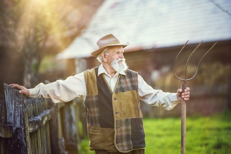 Old farmer with pitchfork taking a break from workの写真素材