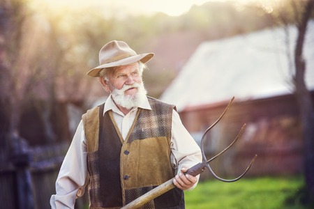 Old farmer with pitchfork taking a break from workの写真素材