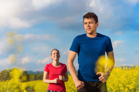 Young couple running outside in spring canola field