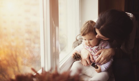 Mother with her baby daughter by the windowの写真素材