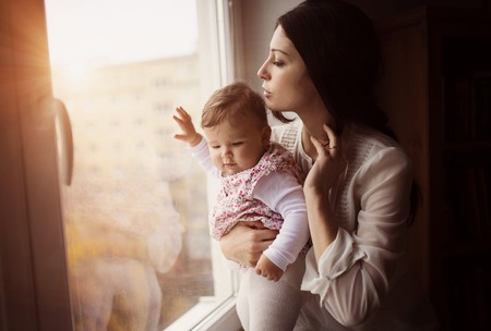 Mother with her baby daughter by the windowの写真素材