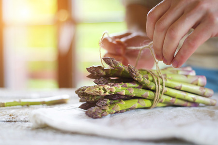 Bunch of fresh green asparagus spears tied with twine on a rustic wooden tableの写真素材