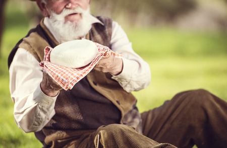 Senior farmer with organic cheese outside in green natureの写真素材
