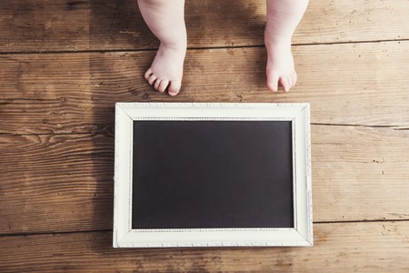 Little baby with empty picture frame on wooden backgroundの写真素材