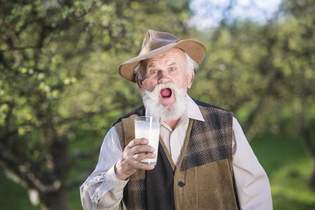 Senior farmer with a glass of milk outside in green natureの写真素材