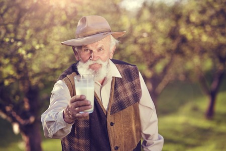 Senior farmer with a glass of milk outside in green natureの写真素材
