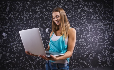 Beautiful young school girl with notebook in front of big blackboard