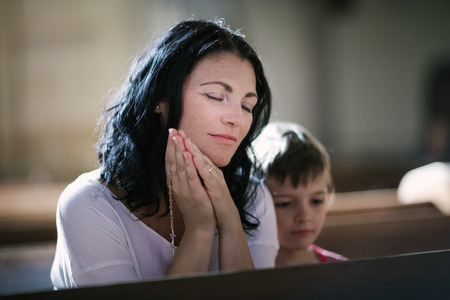 Beautiful woman with her son praying in the churchの写真素材