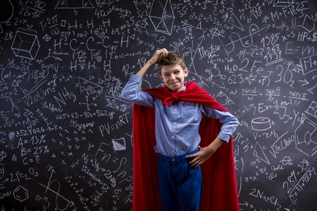 Young handsome school boy with red cape in front of big blackboardの写真素材