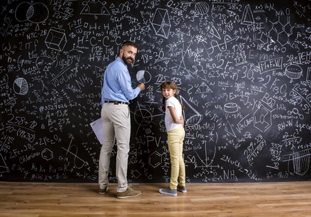 Young hipster school teacher with his pupil in front of big blackboardの写真素材